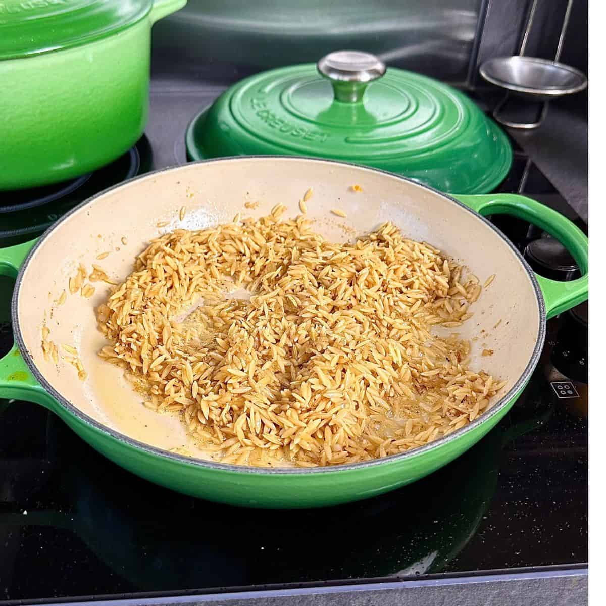 A large green pan containing orzo pasta frying in brown butter. For a pumpkin orzo recipe.
