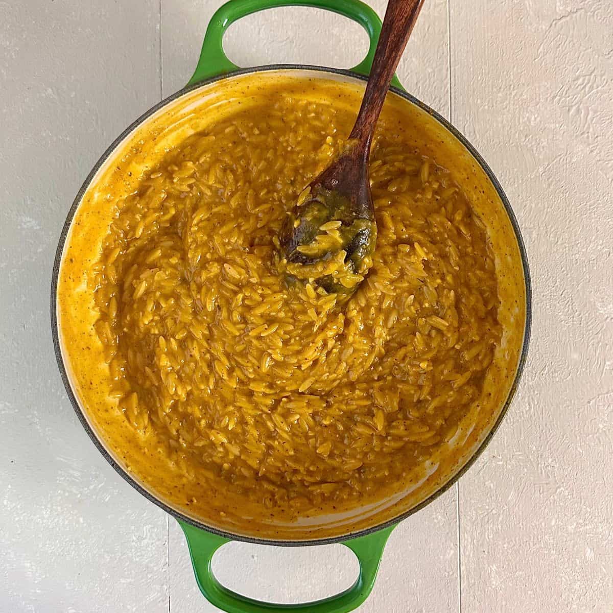 A large green pan containing orzo pasta cooked in a pumpkin puree and vegetable stock, after cooking, ready to serve. Pumpkin orzo recipe.