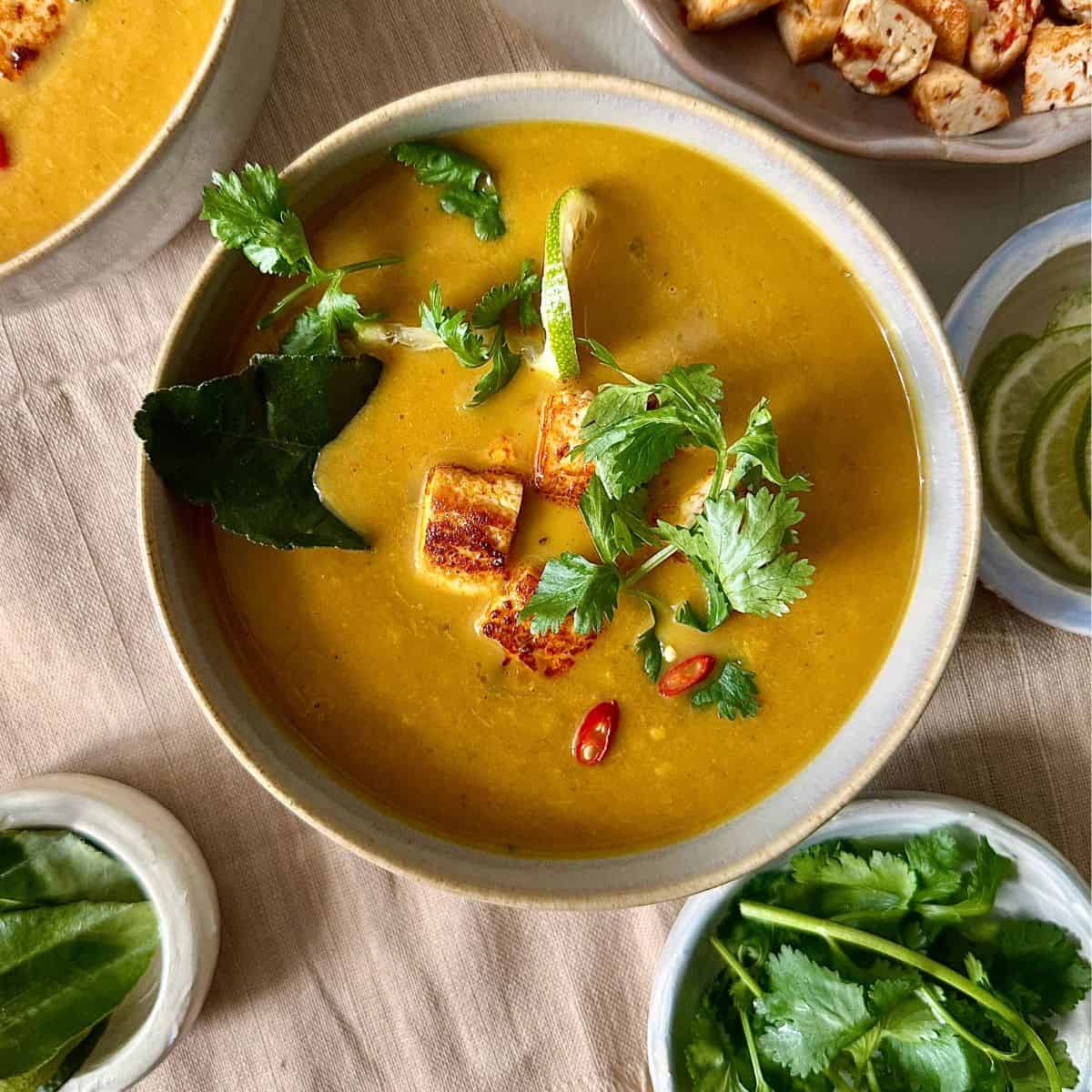 A beige bowl containing Thai pumpkin soup with smoked tofu. Garnished with coriander.