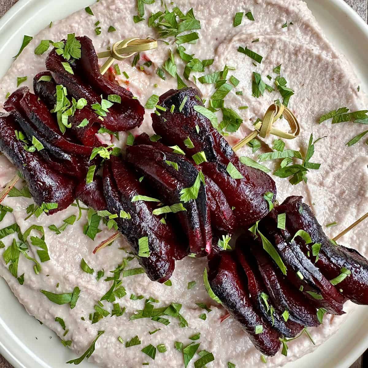 Close-up of beetroot skewers on a bed of borlotti bean dip.