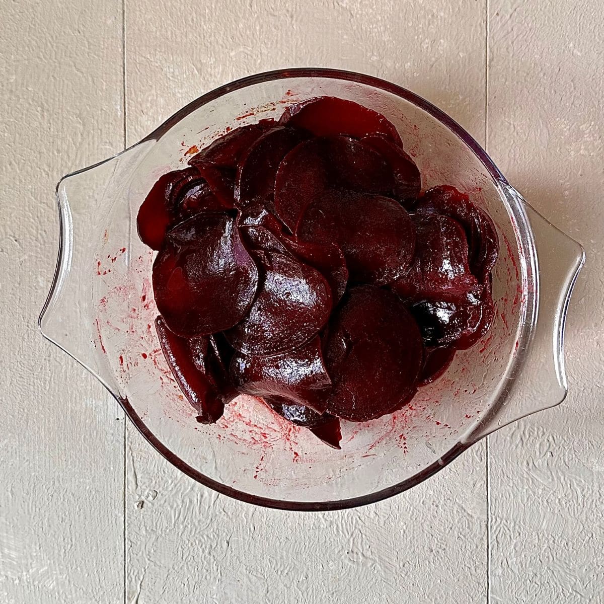 A glass bowl containing thinly sliced cooked beetroot for beetroot skewers.