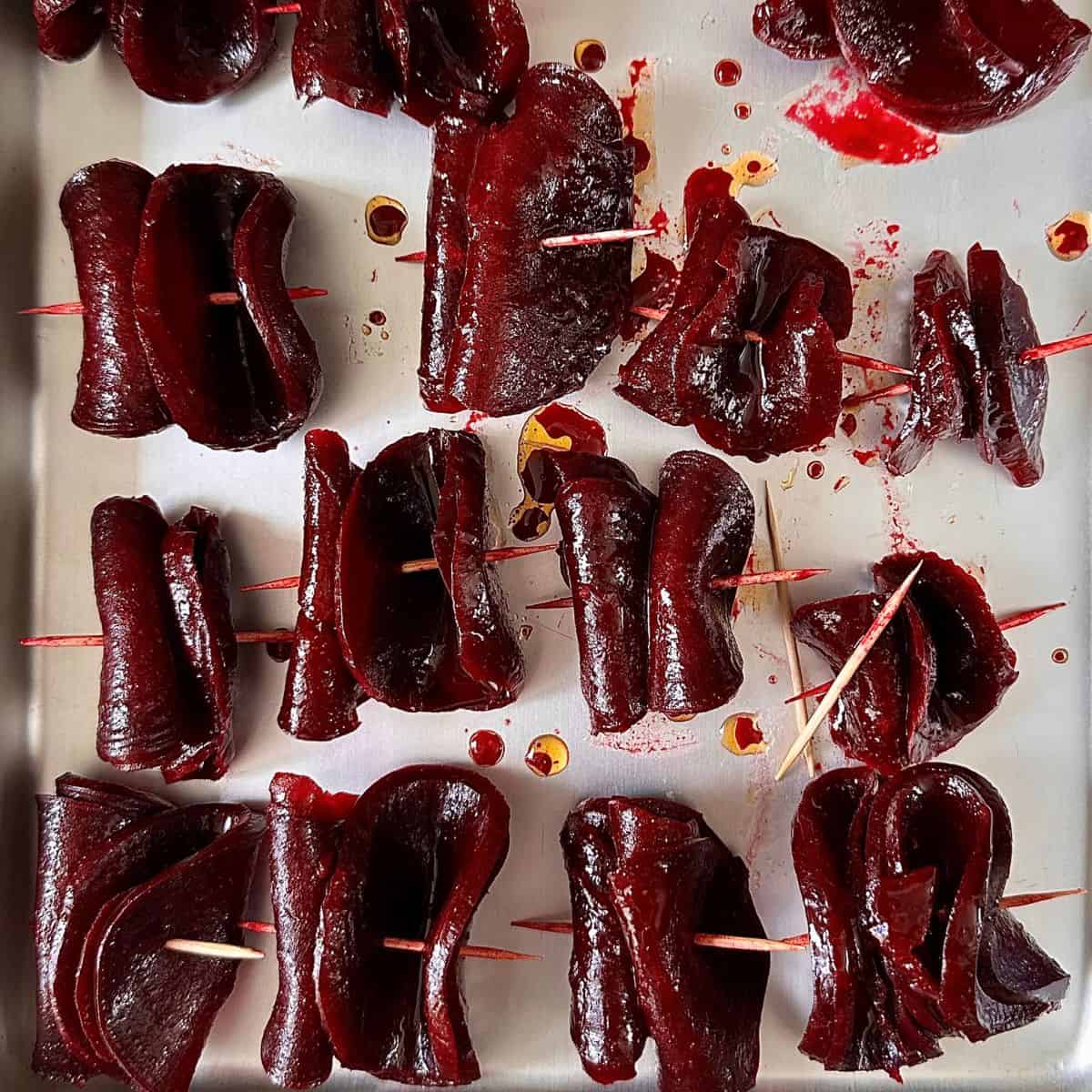A baking tray containing thinly sliced beetroot skewered onto wooden skewers ready for pan frying. For beetroot skewers recipe.