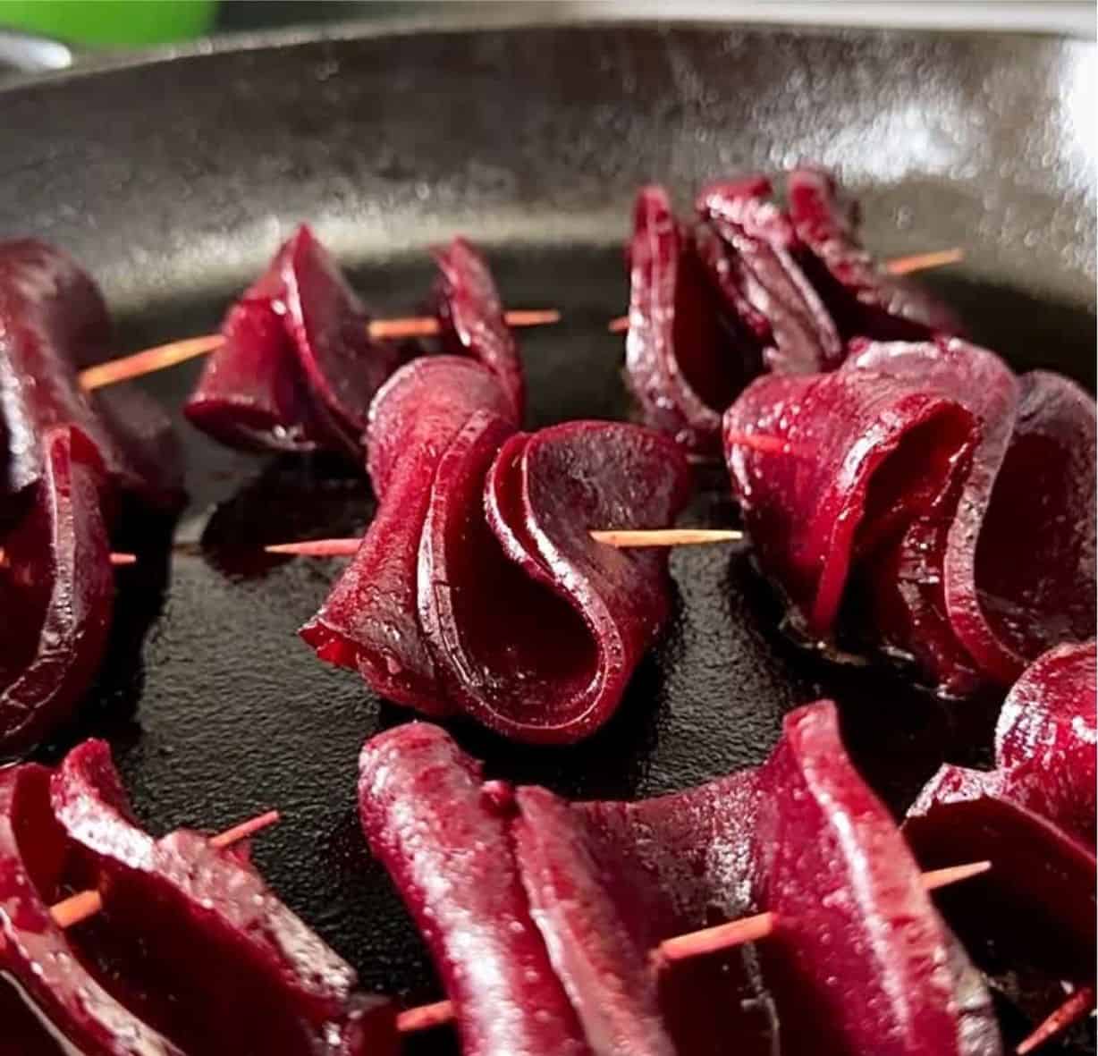 Close up of skewered beetroot in a cast iron pan being seared for abeetroot skewer recipe.