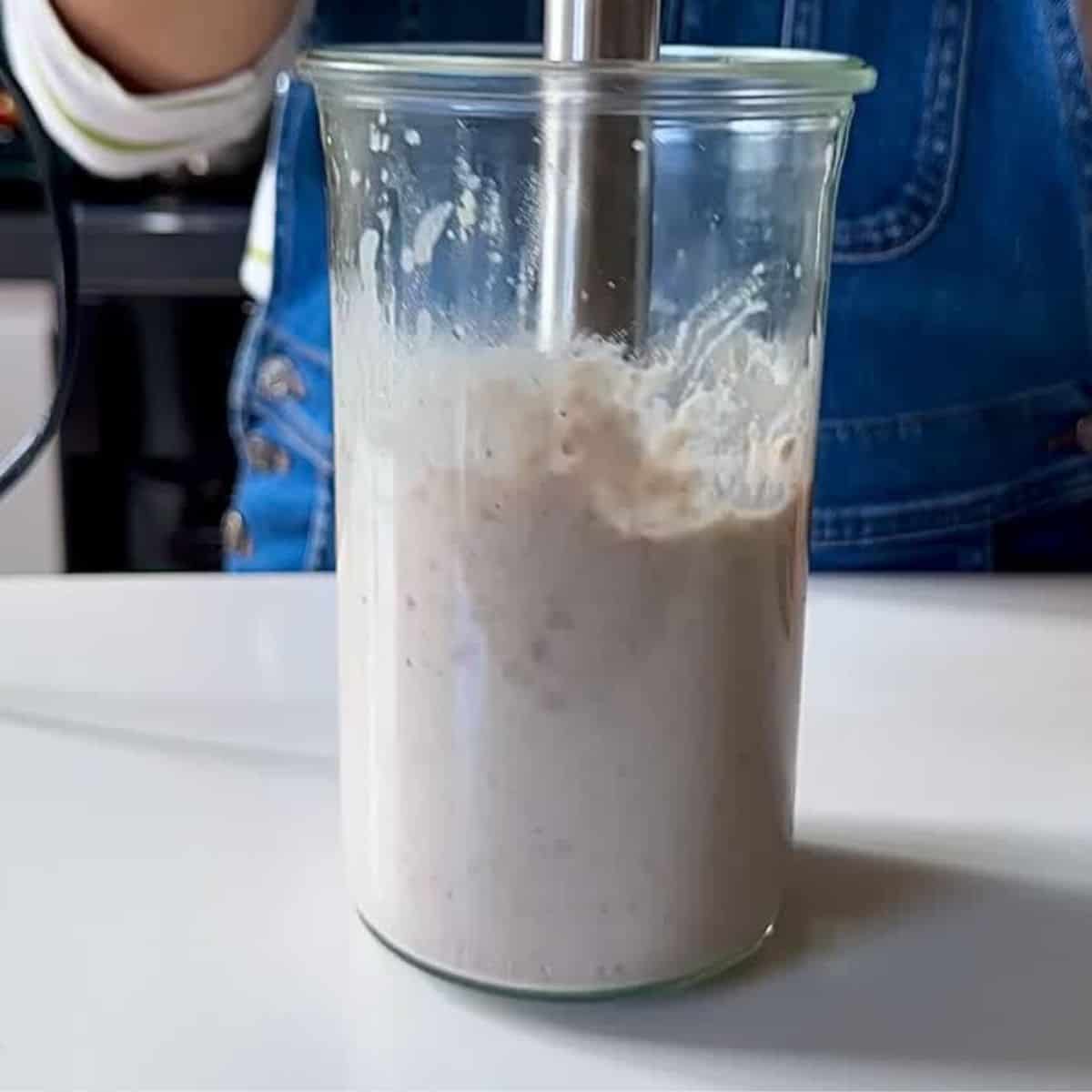 A blender jug containing borlotti beans, tahini, salt, olive oil and lemon juice being blended with a stick blender to make a borlotti bean dip for beetroot skewers.