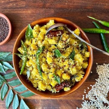 Golden beetroot thoran in a bowl with coconut and curry leaves. The ingredients surround the bowl as decoration.