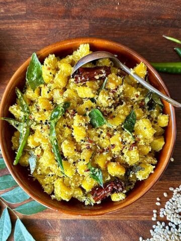 Golden beetroot thoran in a bowl with coconut and curry leaves. The ingredients surround the bowl as decoration.