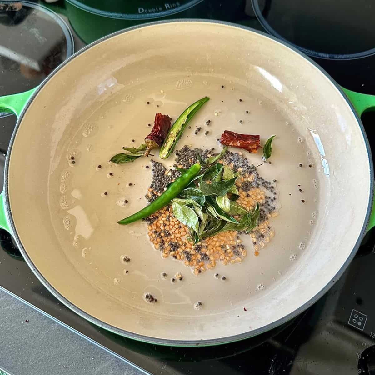 Tempering ingredients: black mustard seeds, urad dal, curry leaves, dried red chilli and green rocket chilli frying in hot oil. For a beetroot thoran recipe.
