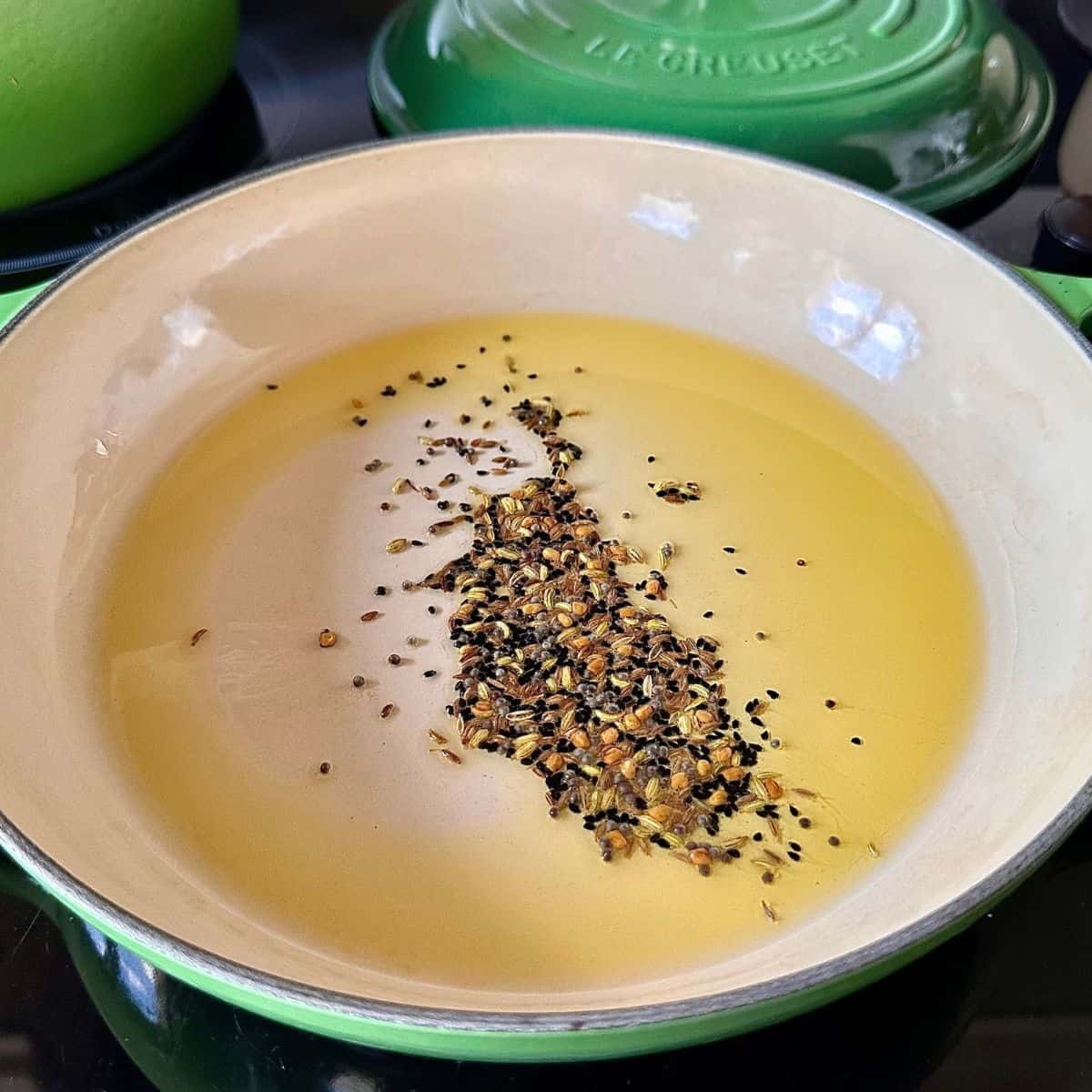 A large green casserole containing Panch phoron frying in mustard oil. For a lal saag recipe.
