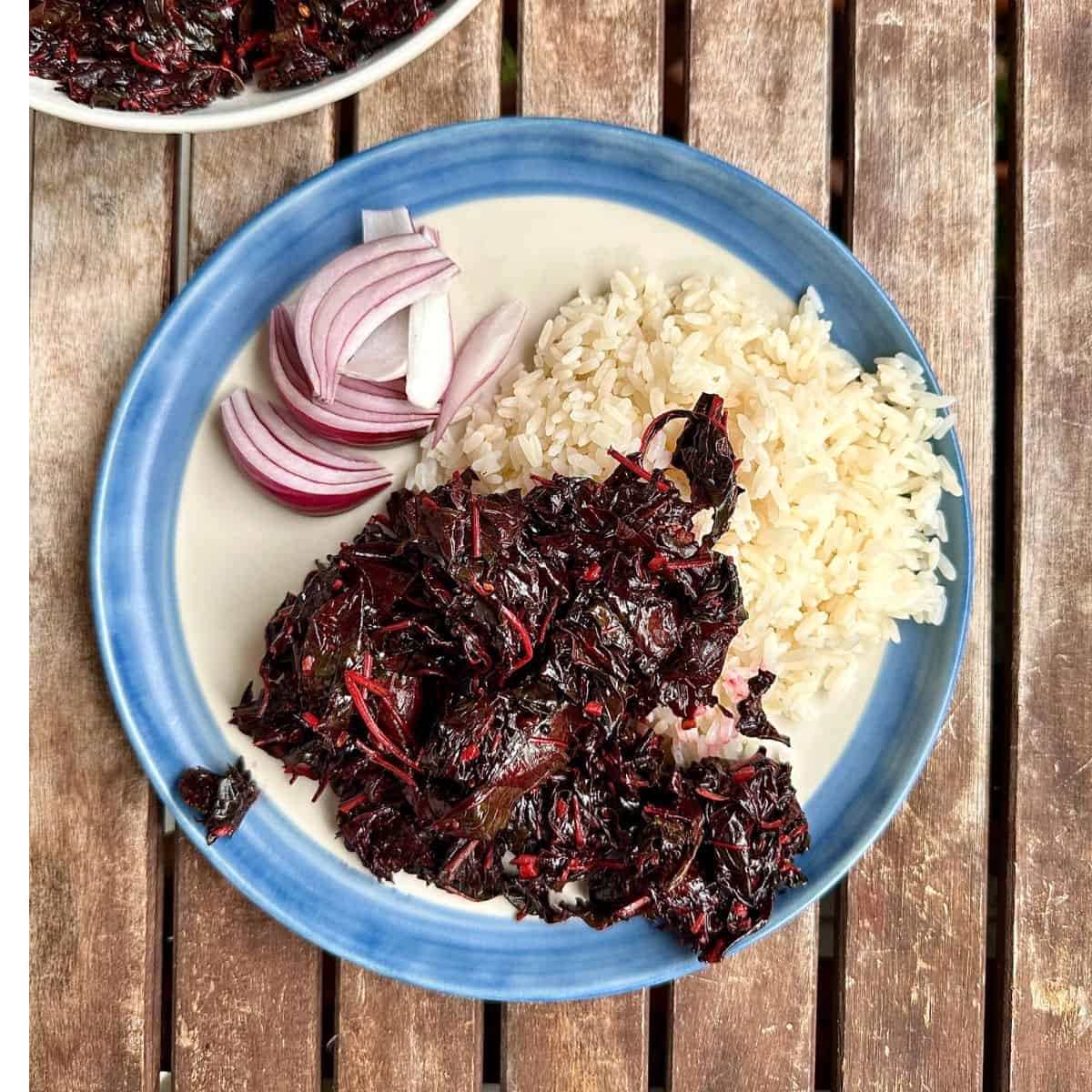 A plate of all saag with steamed rice in a slatted wooden tabletop.