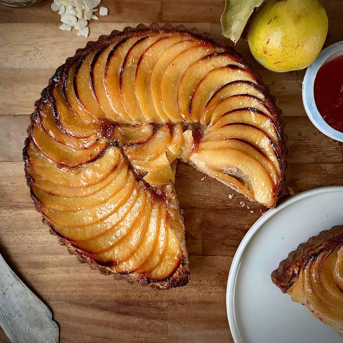 A quince frangipane tart with a slice removed. The slice is on a plate next to the tart.