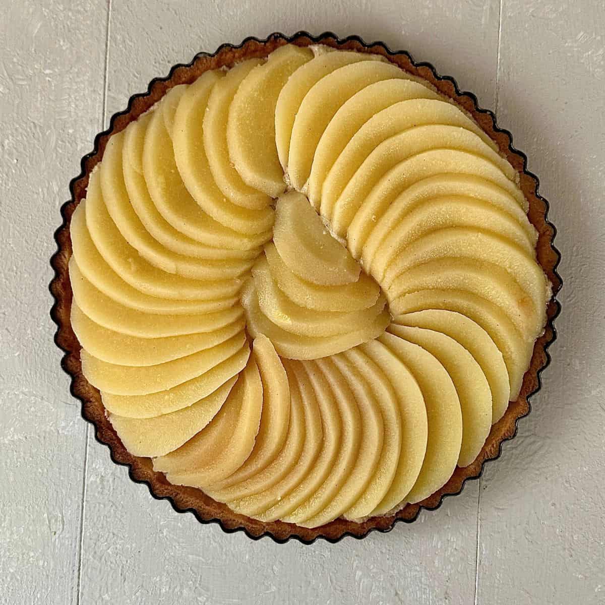 Poached quince slices laid onto a pastry tart base with a layer of frangipane, ready to bake in the oven
