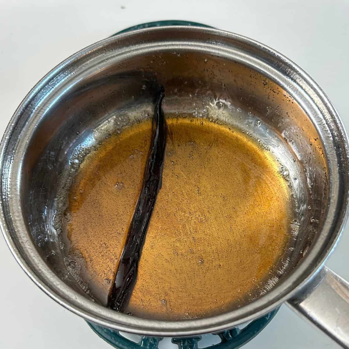A steel saucepan containing the reduced liquid that quinces were poached in. A vanilla pod is in the liquid. To be used as a glaze for a quince frangipane tart.