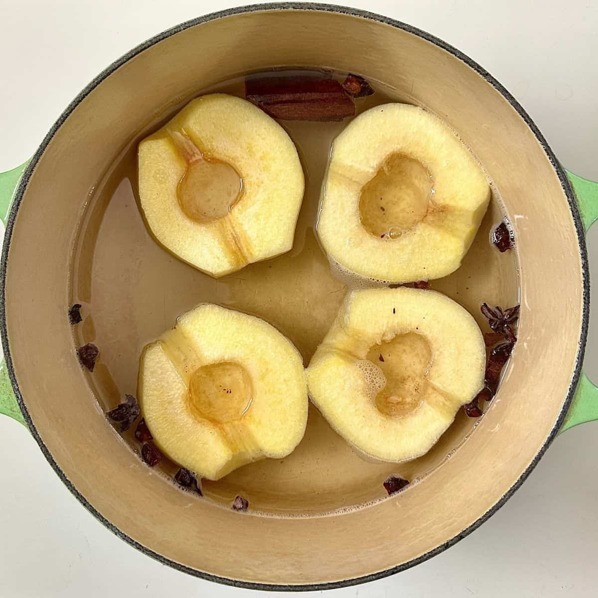 A large green pot with four peeled and cored quince, cut in half in water with dissolved sugar, cinnamon and star anise. For vegan quince frangipane tart recipe.