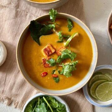 Thai pumpkin soup with smoked tofu in a beige bowl garnished with coriander and birds eye chilli.