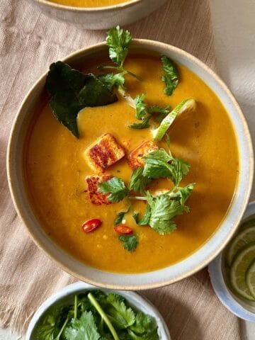 Thai pumpkin soup with smoked tofu in a beige bowl garnished with coriander and birds eye chilli.