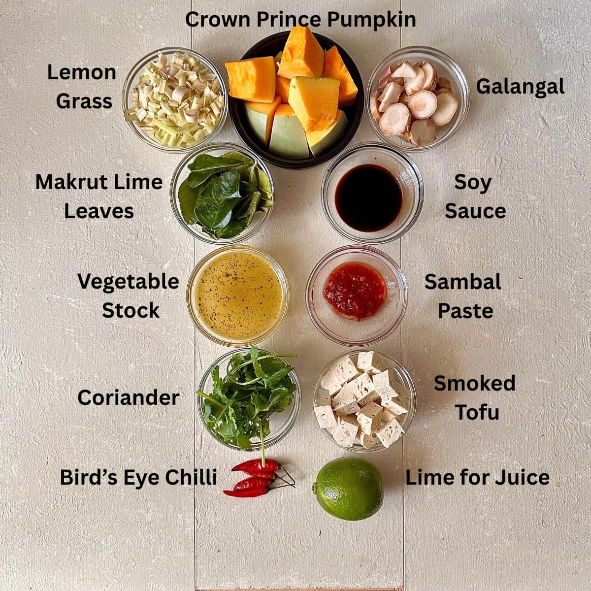 Ingredients for Thai pumpkin soup displayed against a white background in small glass dishes. The ingredients are annotated.