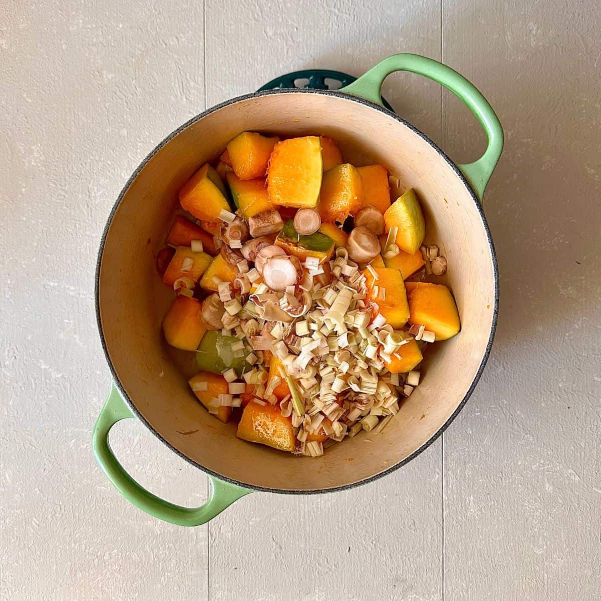 A large green pot containing diced crown prince pumpkin, lemongrass and galangal for a thai pumpkin soup recipe.