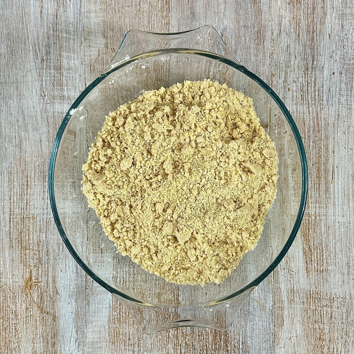 A glass bowl containing pastry mixture at breadcrumb consistency for a vegan quince frangipane tart recipe.