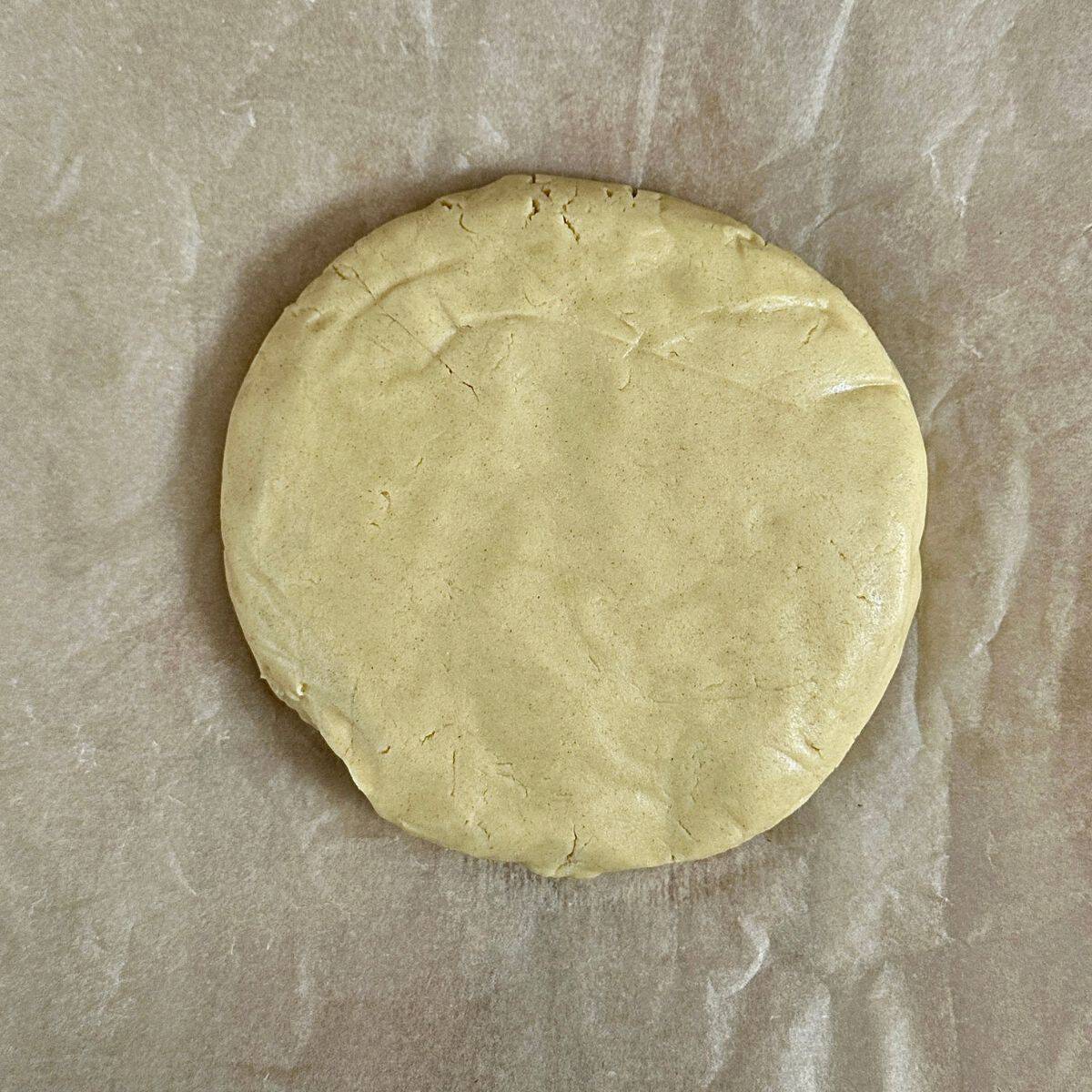 A flattened thick disc of pastry dough, ready to roll, on a piece of parchment paper. For vegan quince frangipane tart recipe.