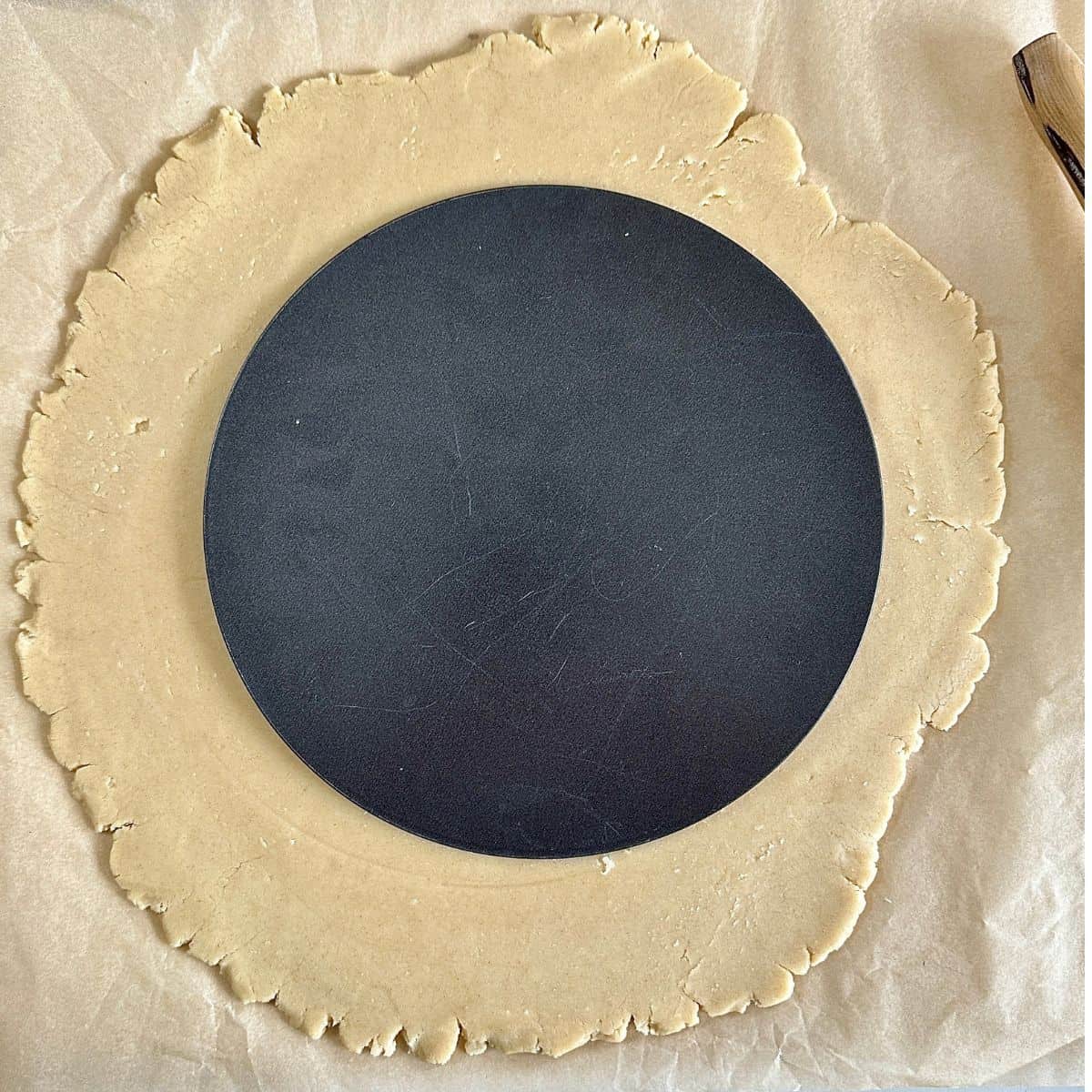Pastry dough for a vegan quince frangipane tart rolled out to a 3mm disc. The inside of a tart tin sits in the centre of the dough to indicate that the dough should be rolled out larger than the tart tin.